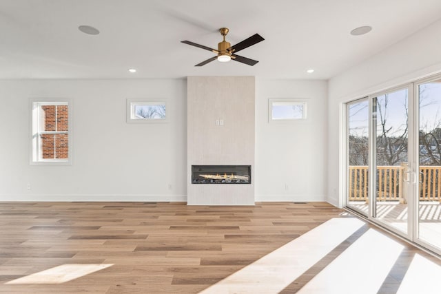 unfurnished living room with a tiled fireplace, ceiling fan, and light wood-type flooring