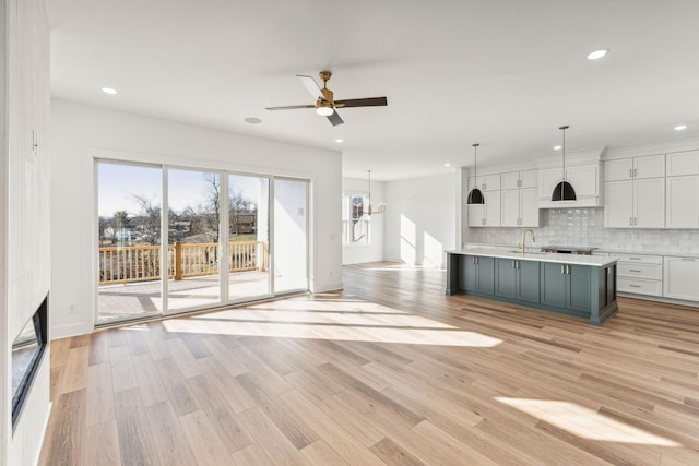 kitchen with pendant lighting, white cabinetry, backsplash, a kitchen island with sink, and light hardwood / wood-style floors