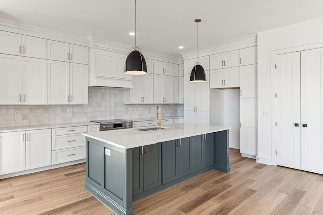 kitchen featuring decorative light fixtures, white cabinetry, an island with sink, sink, and light hardwood / wood-style floors