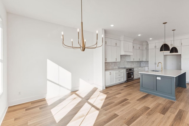 kitchen featuring sink, high end stove, an island with sink, white cabinets, and decorative light fixtures