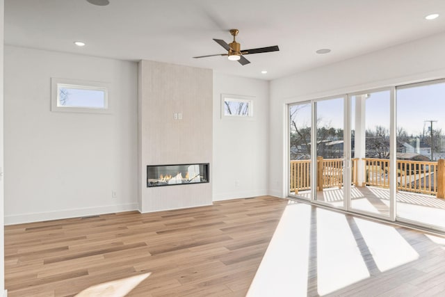 unfurnished living room featuring a tiled fireplace, light hardwood / wood-style flooring, and ceiling fan