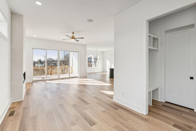 unfurnished living room featuring ceiling fan with notable chandelier and light hardwood / wood-style floors