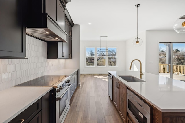 kitchen with sink, appliances with stainless steel finishes, tasteful backsplash, a center island with sink, and decorative light fixtures