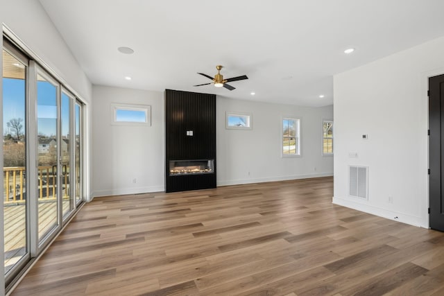 unfurnished living room featuring ceiling fan, a large fireplace, and wood-type flooring