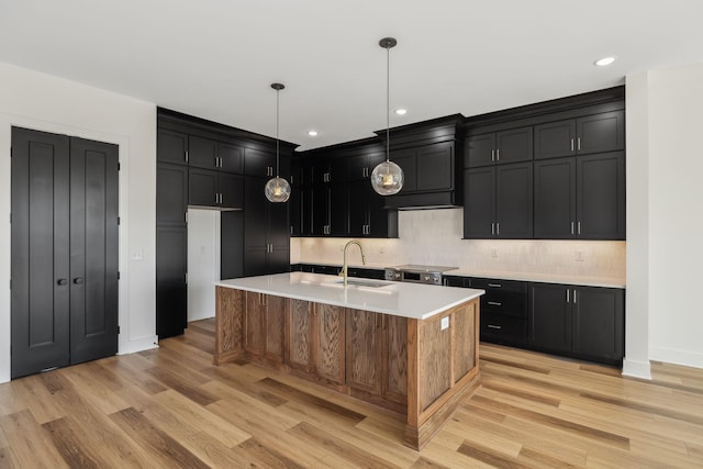 kitchen featuring sink, decorative light fixtures, a center island with sink, light wood-type flooring, and decorative backsplash