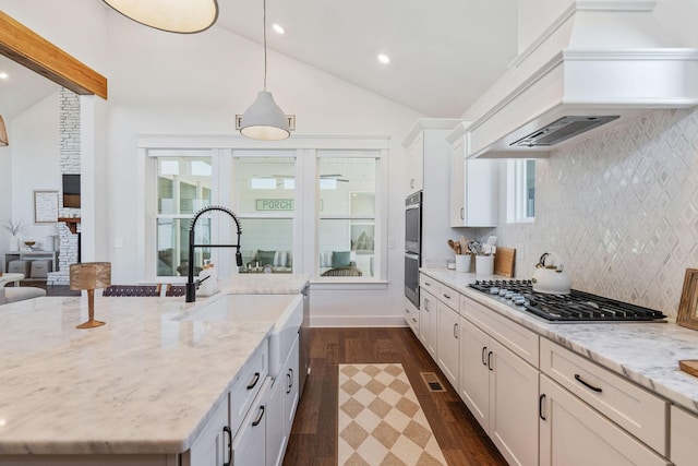 kitchen with hanging light fixtures, appliances with stainless steel finishes, custom range hood, and light stone counters