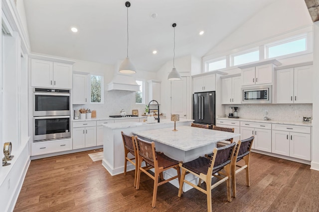 kitchen featuring pendant lighting, a breakfast bar area, appliances with stainless steel finishes, white cabinetry, and a center island with sink