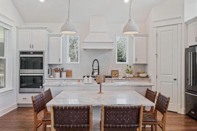 kitchen featuring decorative light fixtures, high end refrigerator, light stone counters, and double oven