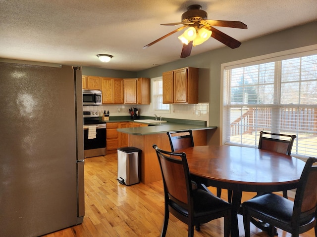 kitchen featuring decorative backsplash, light hardwood / wood-style floors, kitchen peninsula, stainless steel appliances, and a textured ceiling