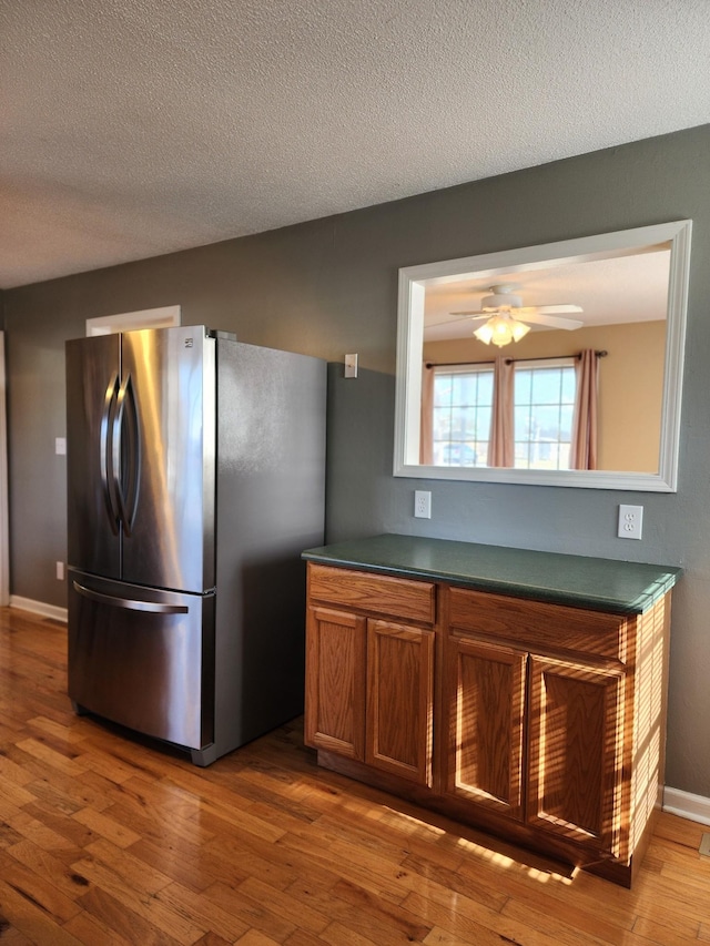 kitchen featuring ceiling fan, a textured ceiling, stainless steel fridge, and light wood-type flooring