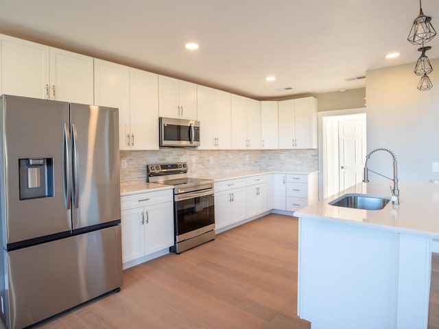 kitchen featuring sink, white cabinetry, stainless steel appliances, decorative light fixtures, and light wood-type flooring