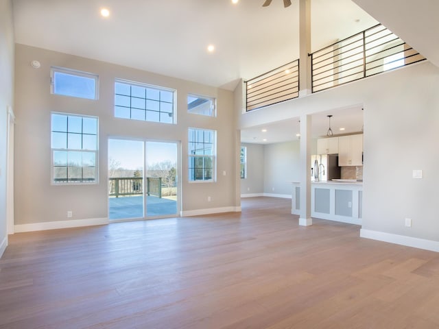 unfurnished living room featuring a high ceiling, ceiling fan, and light hardwood / wood-style floors