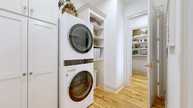 laundry area featuring cabinets, stacked washer and clothes dryer, and light hardwood / wood-style flooring