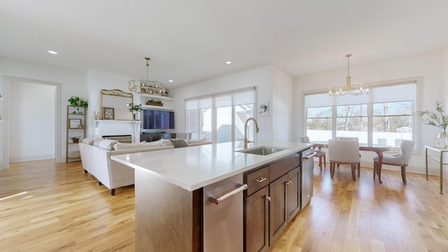 kitchen with sink, a notable chandelier, light hardwood / wood-style floors, a center island with sink, and decorative light fixtures