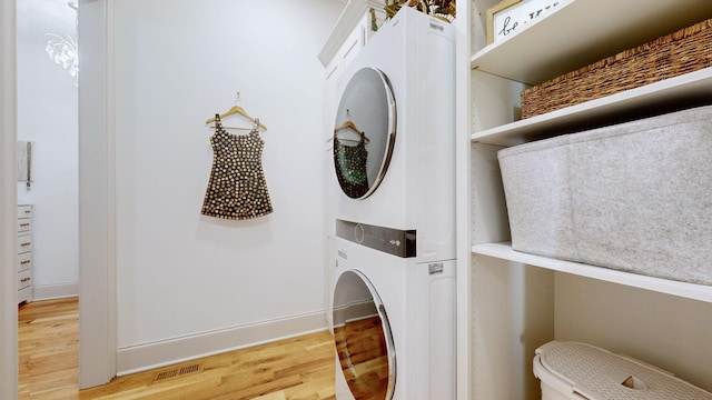 laundry area with hardwood / wood-style flooring and stacked washer and clothes dryer