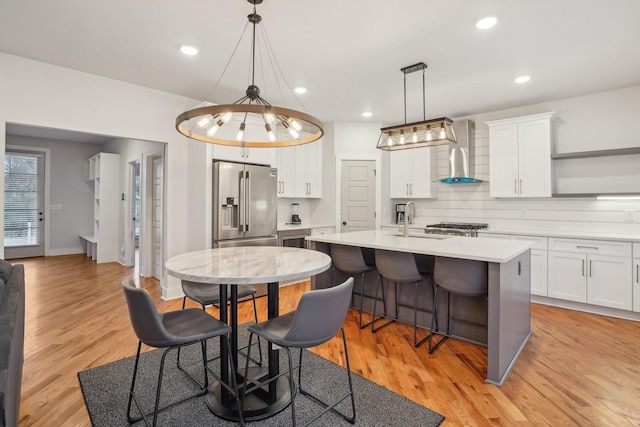 kitchen featuring high quality fridge, white cabinetry, a breakfast bar area, a kitchen island with sink, and wall chimney exhaust hood