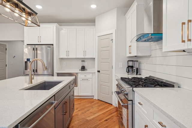 kitchen featuring wall chimney exhaust hood, sink, high end appliances, white cabinetry, and decorative light fixtures