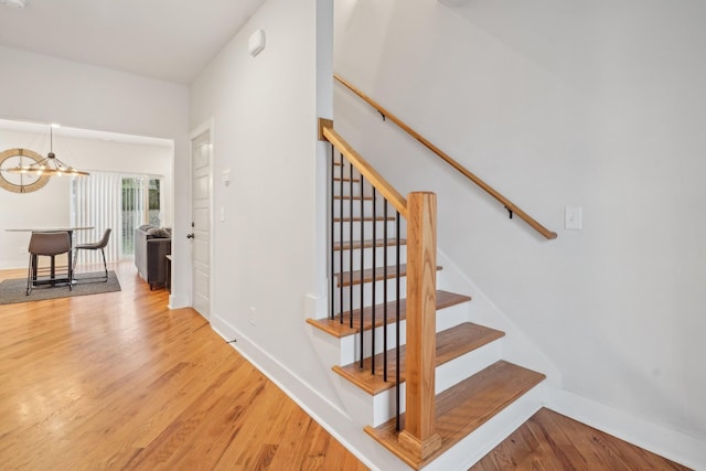 stairway with wood-type flooring and a notable chandelier