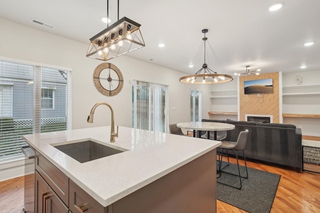 kitchen featuring sink, a large fireplace, hanging light fixtures, and a center island with sink