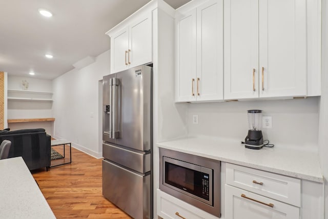 kitchen featuring light stone countertops, light hardwood / wood-style floors, white cabinets, and appliances with stainless steel finishes