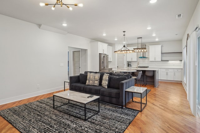 living room with sink, an inviting chandelier, and light wood-type flooring