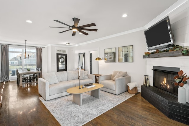 living room with crown molding, a brick fireplace, dark hardwood / wood-style floors, and ceiling fan with notable chandelier