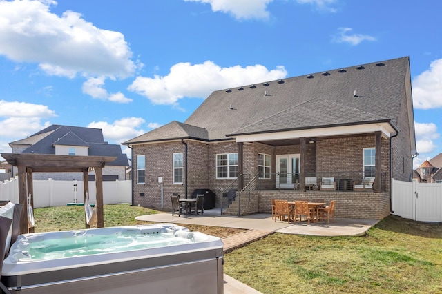 rear view of property featuring a hot tub, a lawn, and a patio area