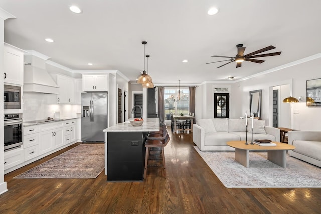 kitchen featuring premium range hood, appliances with stainless steel finishes, light stone countertops, an island with sink, and white cabinets