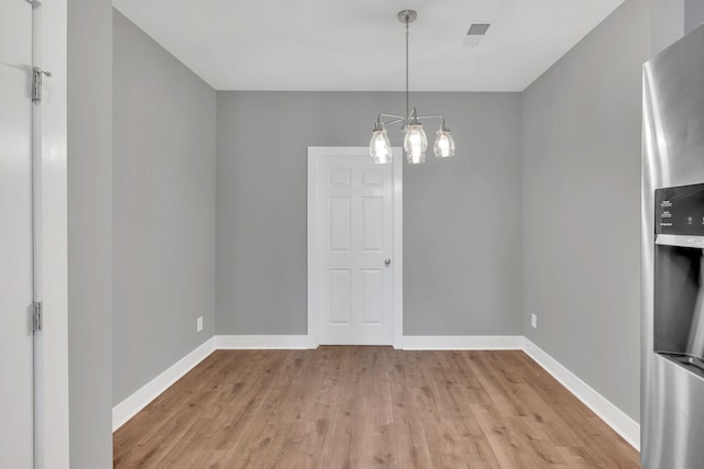 unfurnished dining area with a chandelier and light wood-type flooring