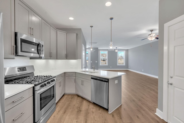 kitchen with pendant lighting, gray cabinets, kitchen peninsula, and appliances with stainless steel finishes