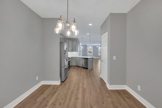 kitchen featuring appliances with stainless steel finishes, gray cabinetry, pendant lighting, and light hardwood / wood-style flooring