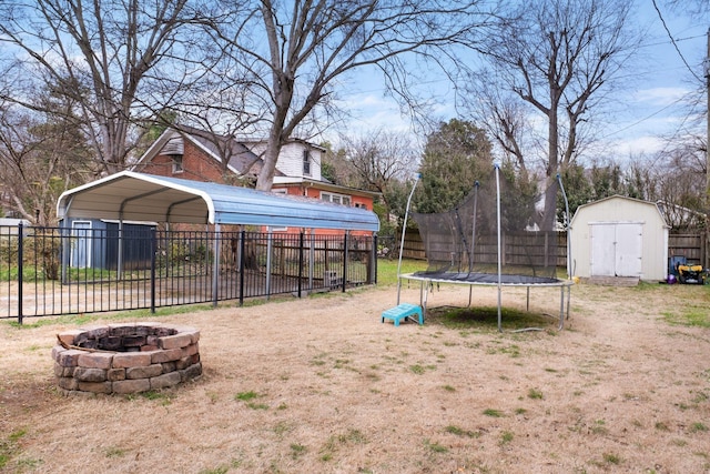 view of yard featuring a trampoline, a storage shed, a carport, and an outdoor fire pit