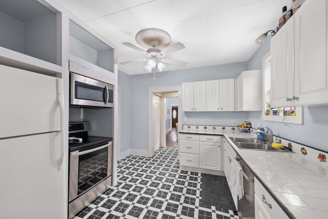 kitchen with tile countertops, white cabinetry, sink, ceiling fan, and stainless steel appliances