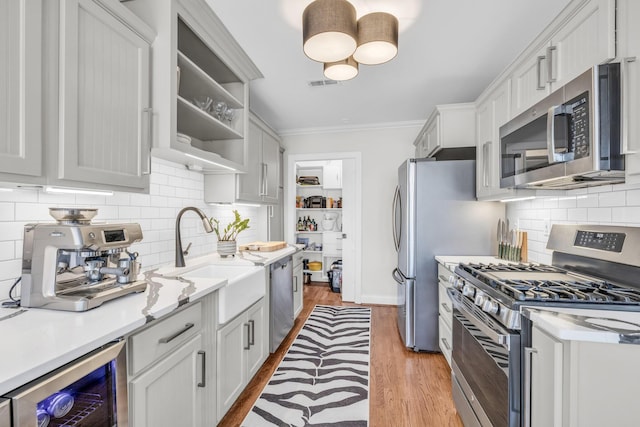 kitchen featuring sink, crown molding, appliances with stainless steel finishes, white cabinetry, and wine cooler