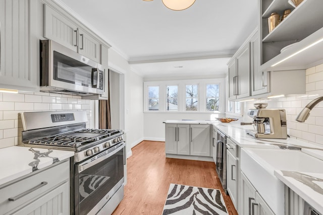 kitchen with sink, crown molding, appliances with stainless steel finishes, gray cabinetry, and light wood-type flooring