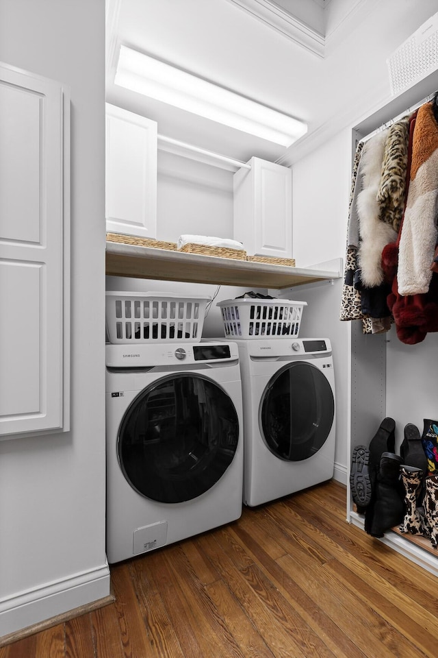 clothes washing area with dark wood-type flooring, washing machine and clothes dryer, and cabinets