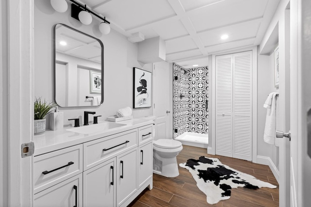 bathroom with coffered ceiling, tiled shower, vanity, and toilet