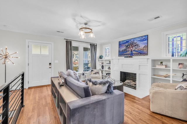 living room with crown molding, a brick fireplace, a healthy amount of sunlight, and light hardwood / wood-style flooring