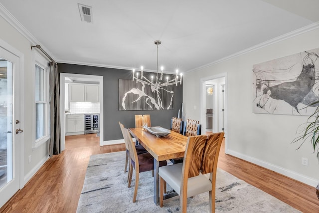 dining room featuring wine cooler, a notable chandelier, crown molding, and light hardwood / wood-style floors