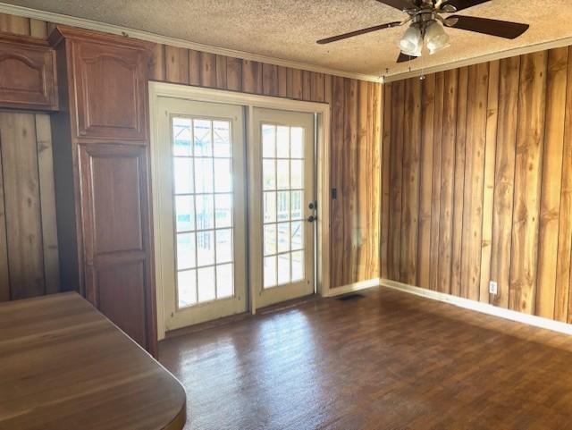 entryway with dark wood-type flooring, crown molding, wooden walls, and a textured ceiling