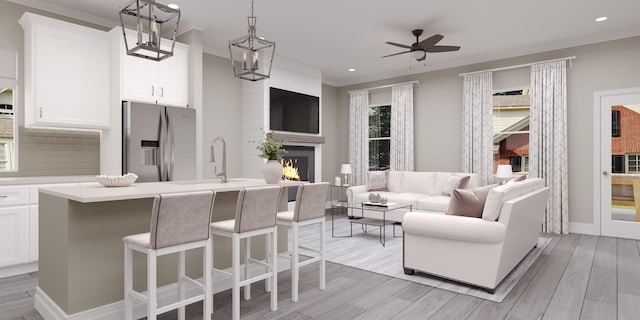 kitchen featuring decorative light fixtures, white cabinetry, stainless steel fridge, a center island with sink, and light hardwood / wood-style flooring