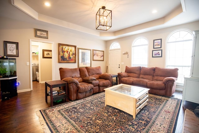 living room with an inviting chandelier, a tray ceiling, and dark hardwood / wood-style flooring