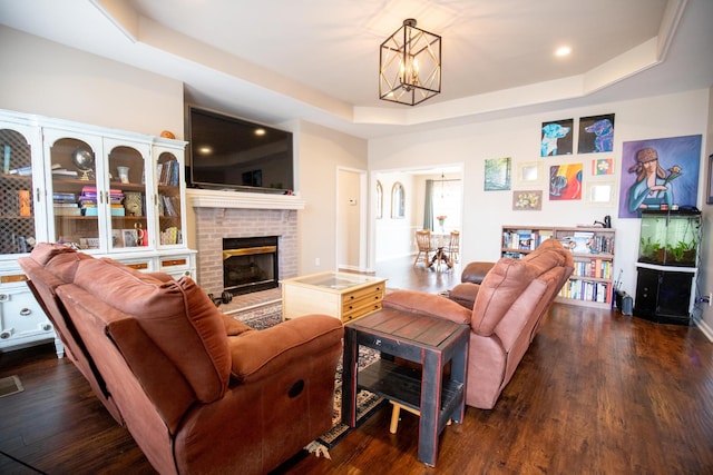 living room featuring an inviting chandelier, a brick fireplace, dark hardwood / wood-style floors, and a raised ceiling