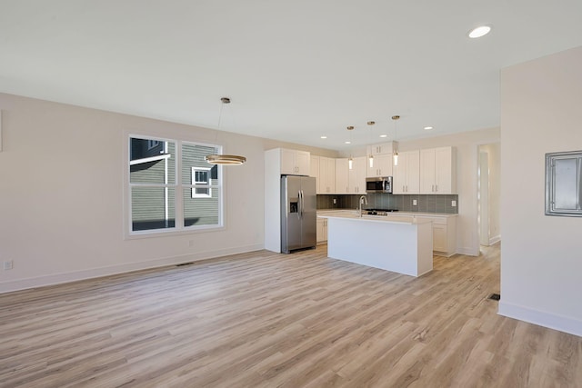 kitchen with stainless steel appliances, white cabinets, light countertops, decorative backsplash, and a center island with sink