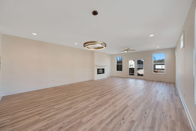 unfurnished living room with light wood-type flooring, a glass covered fireplace, and baseboards