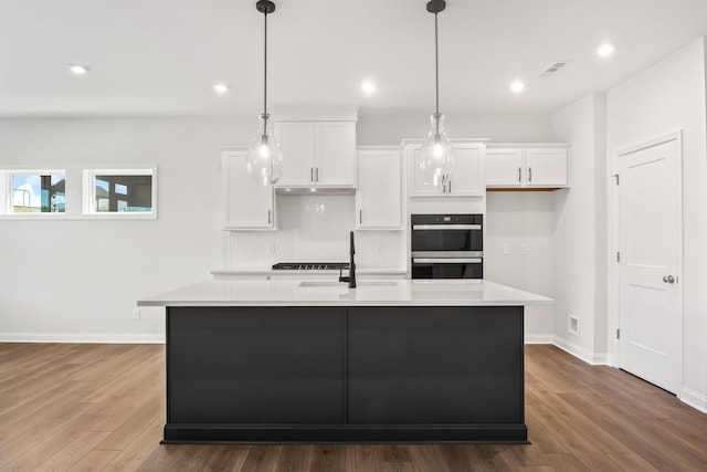 kitchen with pendant lighting, dark wood-type flooring, a center island with sink, and white cabinets