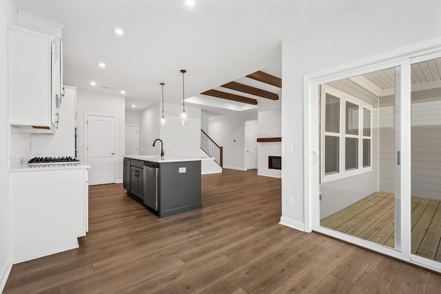 kitchen with dark hardwood / wood-style floors, a fireplace, decorative light fixtures, white cabinetry, and an island with sink