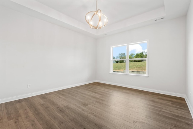 unfurnished room featuring dark hardwood / wood-style floors, a notable chandelier, and a tray ceiling