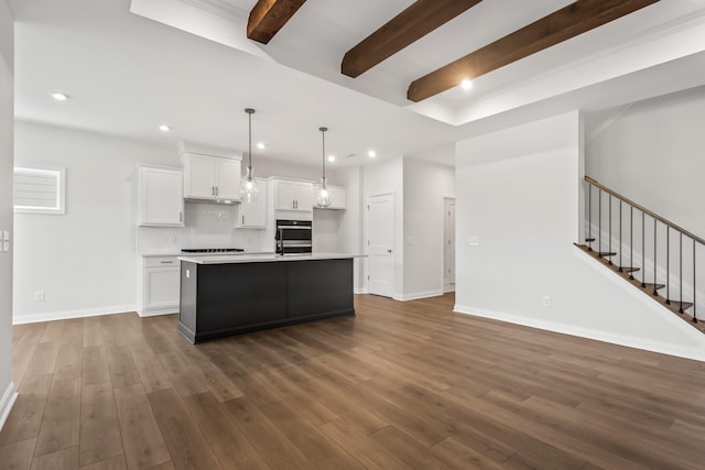 kitchen featuring dark hardwood / wood-style floors, decorative light fixtures, beamed ceiling, white cabinetry, and a center island with sink