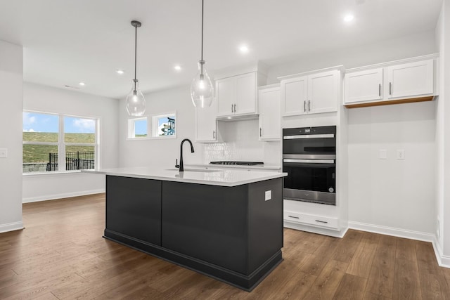 kitchen with decorative light fixtures, white cabinetry, sink, double wall oven, and a kitchen island with sink